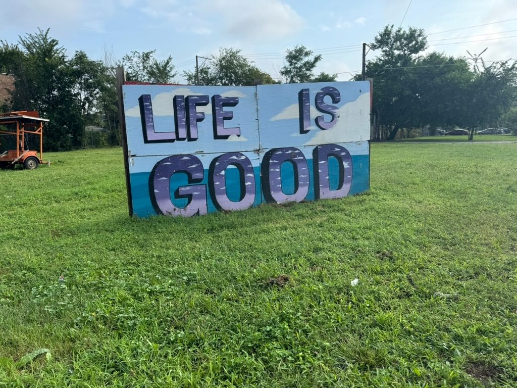 A hand-painted 'Life is Good' sign standing in a grassy Pittsburgh lot